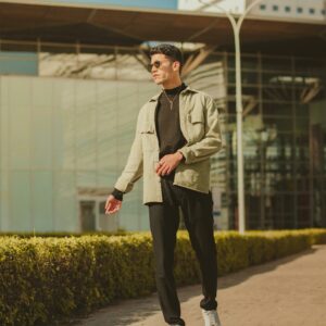 A fashionable man in sunglasses walks confidently outdoors in an urban architectural setting.